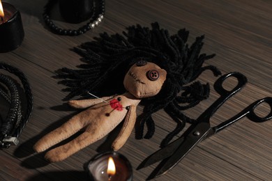 Photo of Voodoo doll with pins, scissors and burning candles on wooden table