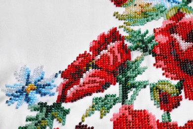 Photo of Beautiful floral bead embroidery on white fabric, closeup