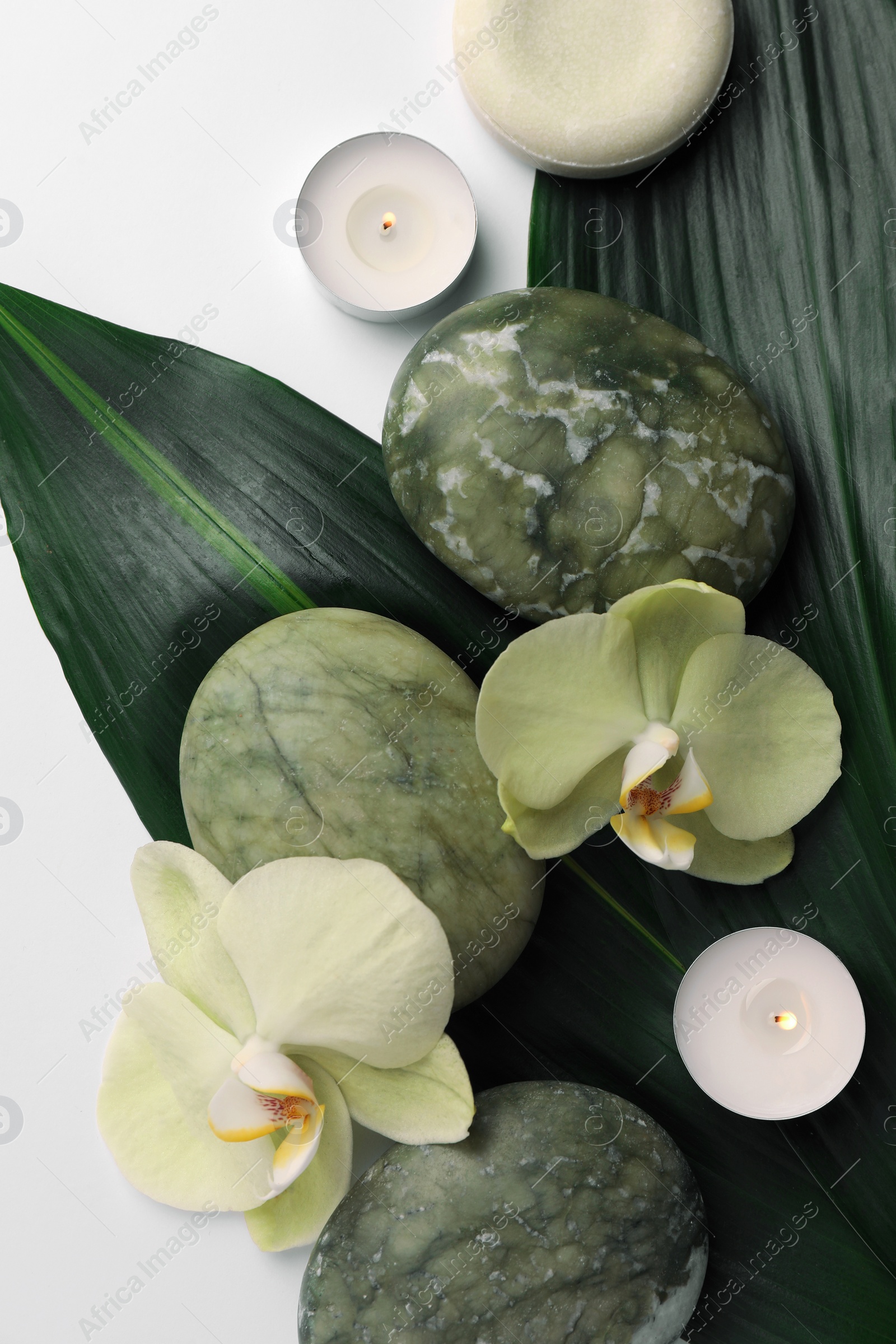 Photo of Flat lay composition with spa stones, green leaves and beautiful flowers on white table