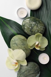 Flat lay composition with spa stones, green leaves and beautiful flowers on white table