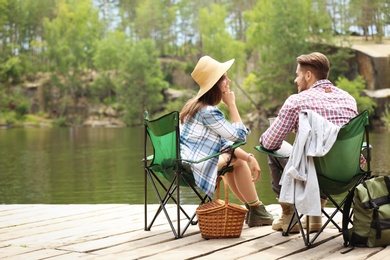 Photo of Young couple resting on pier near lake. Camping season