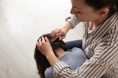 Photo of Mother examining her daughter's hair indoors. Anti lice treatment