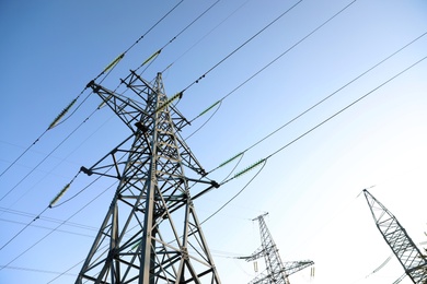 Photo of High voltage tower against blue sky on sunny day, low angle view