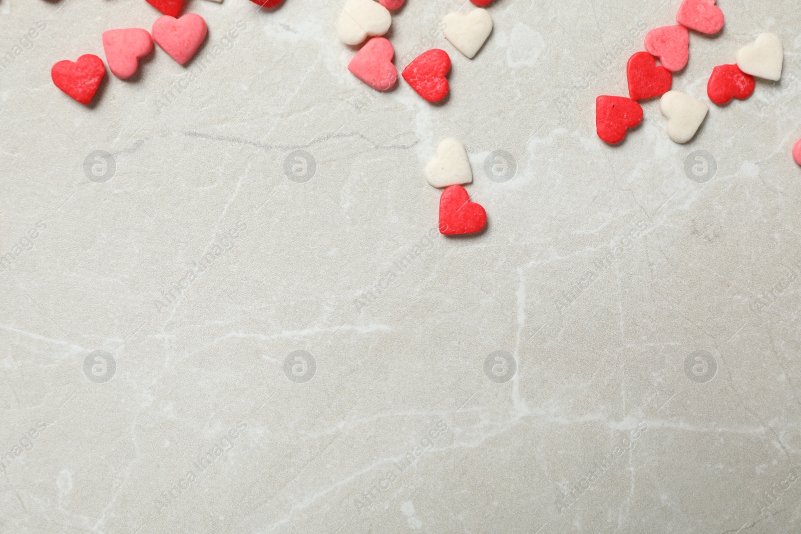 Photo of Bright heart shaped sprinkles on light grey table, flat lay. Space for text