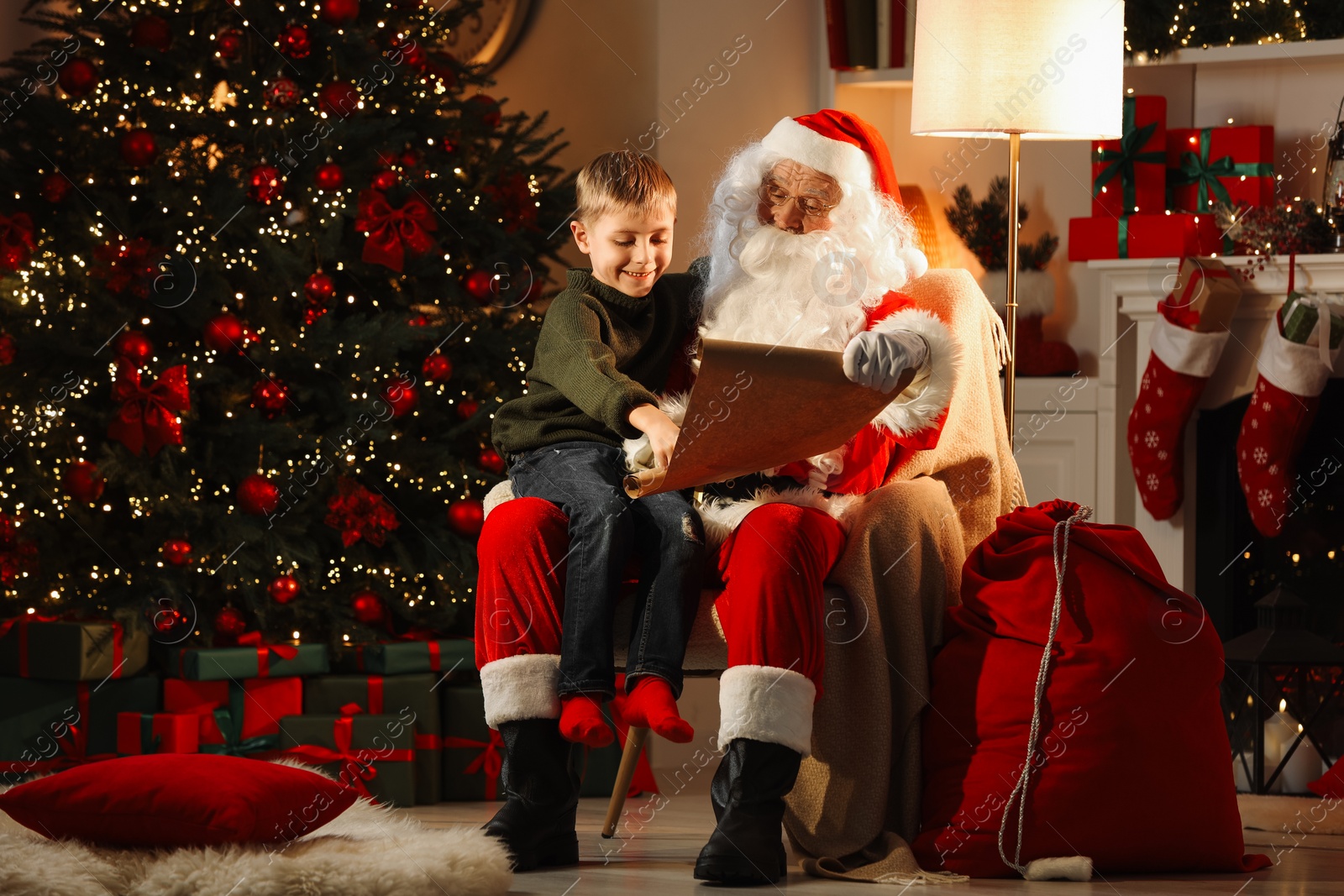 Photo of Merry Christmas. Santa Claus with little boy reading letter at home
