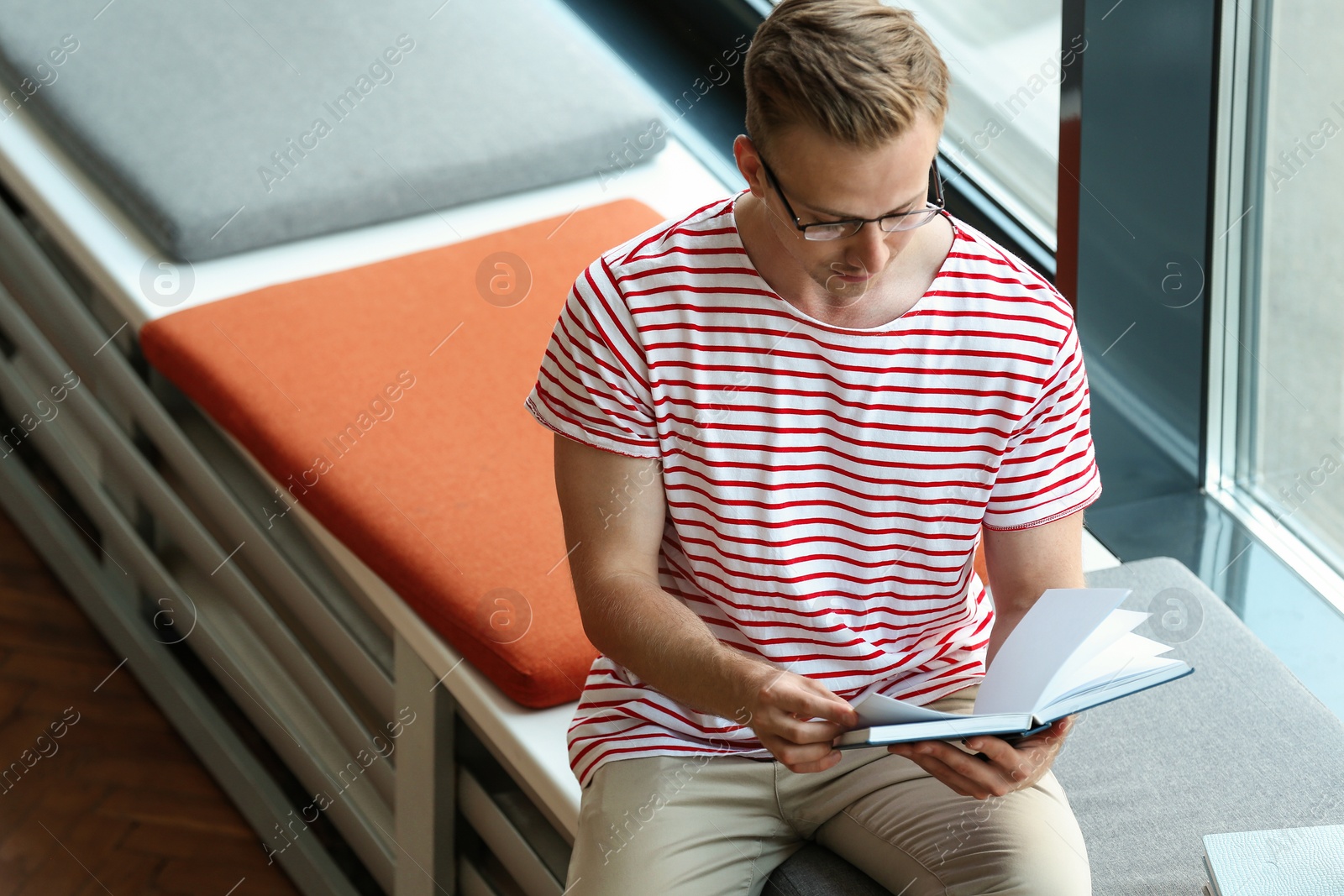 Photo of Young man reading book near window in library