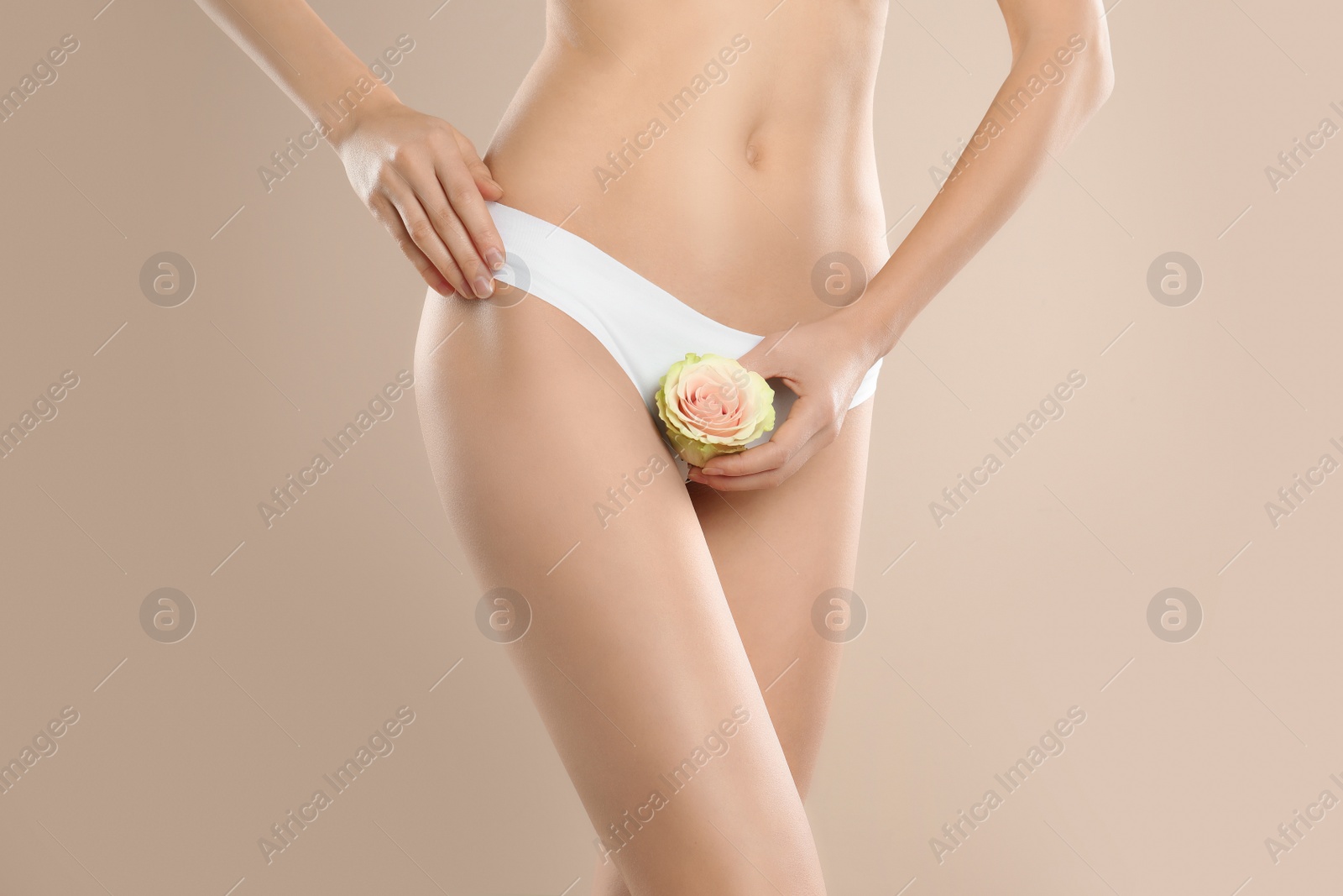 Photo of Woman with flower showing smooth skin after bikini epilation on beige background, closeup. Body care concept