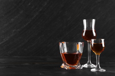 Different delicious liqueurs in glasses on black wooden table, space for text