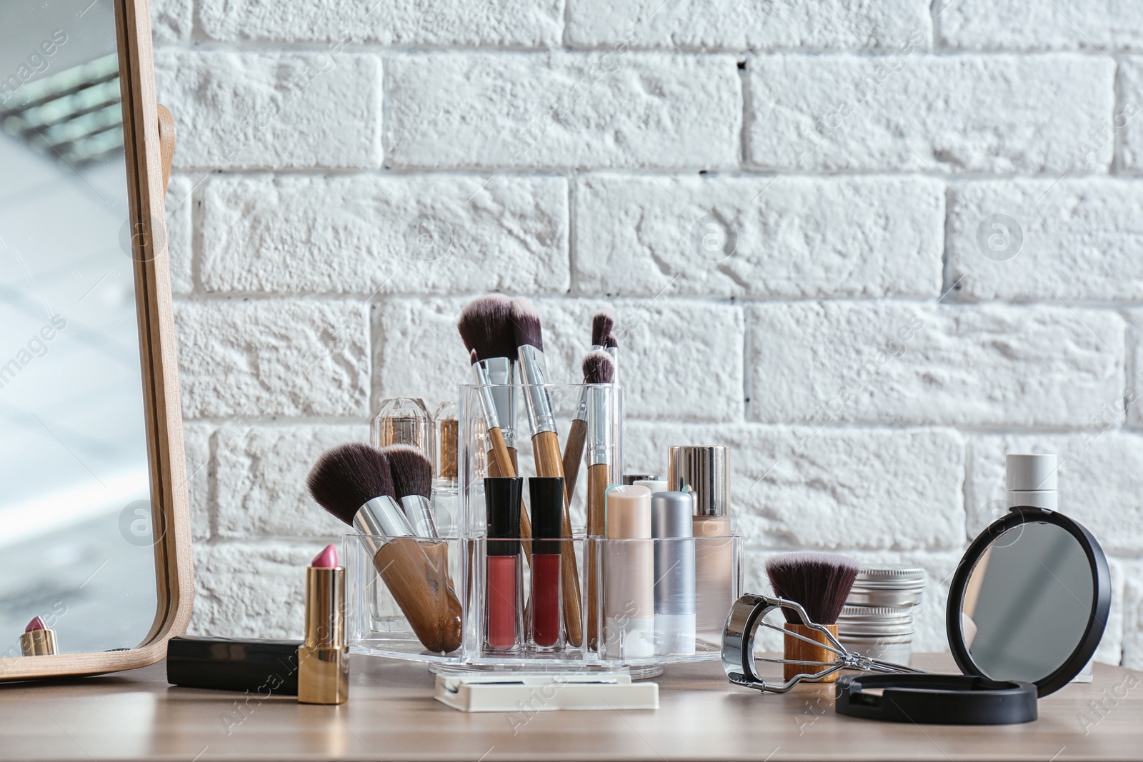 Photo of Organizer with cosmetic products for makeup on table near brick wall