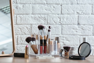 Photo of Organizer with cosmetic products for makeup on table near brick wall