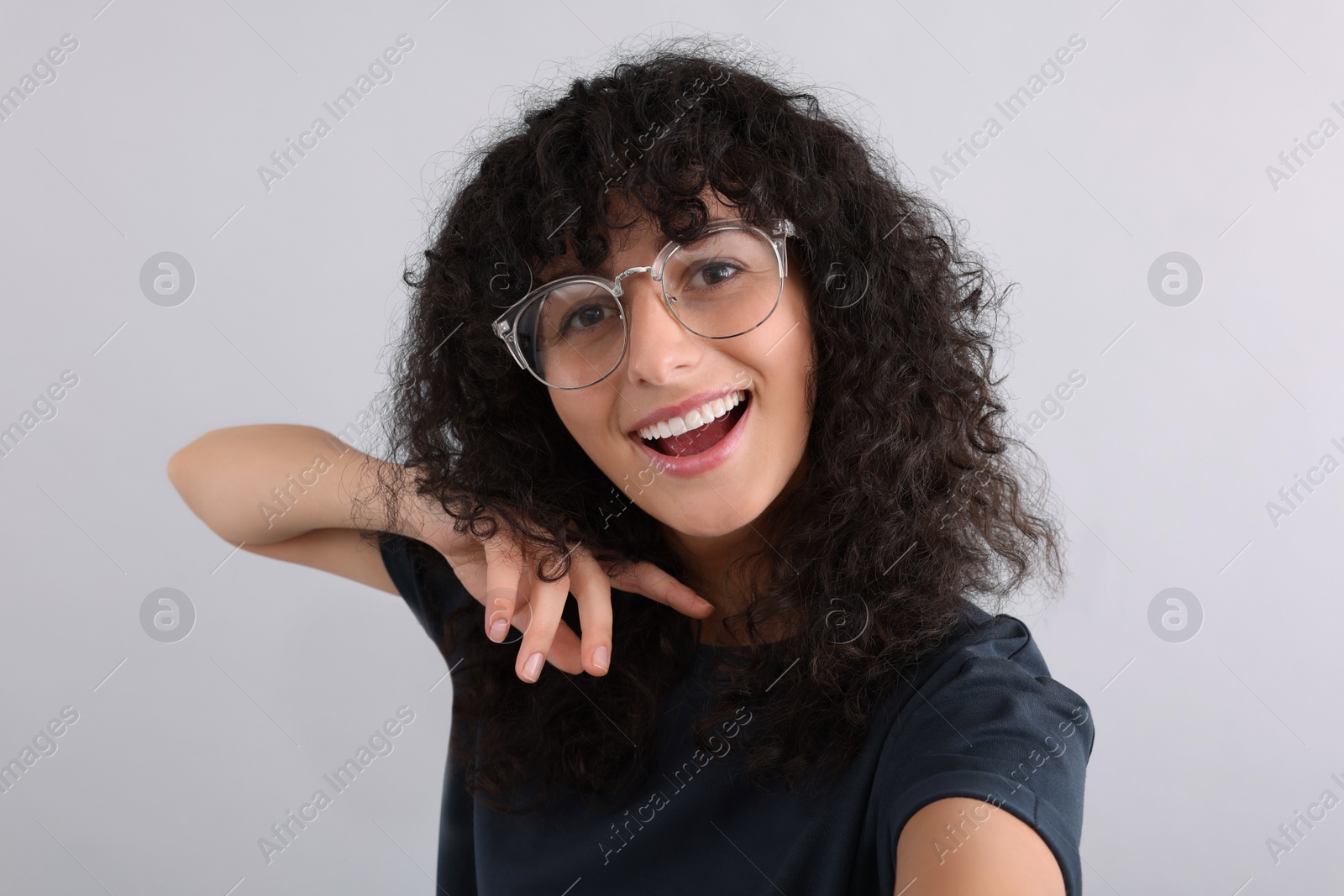 Photo of Beautiful young woman in eyeglasses taking selfie on light grey background