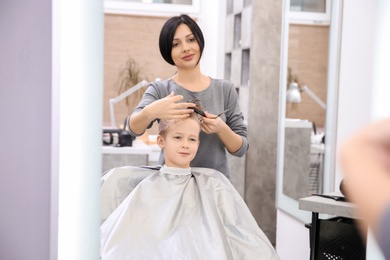 Photo of Professional female hairdresser working with little boy in salon