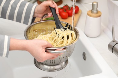 Photo of Woman rinsing pasta in colander above sink, closeup