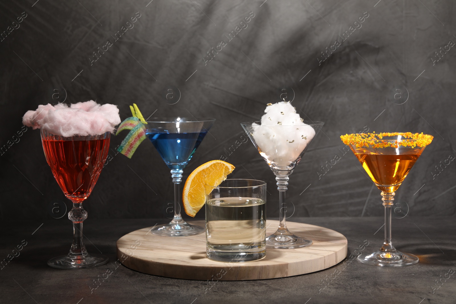 Photo of Tasty cotton candy cocktail and other alcoholic drinks in glasses on gray textured table