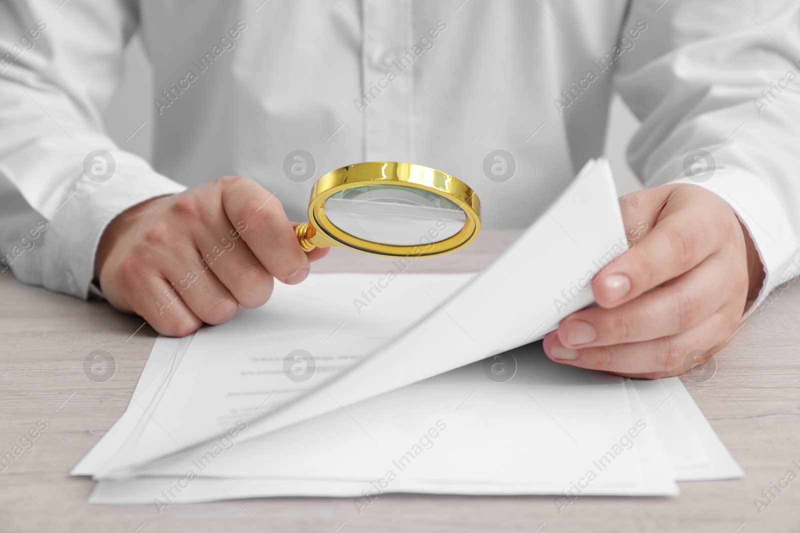 Photo of Man looking at document through magnifier at white wooden table, closeup. Searching concept