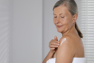 Photo of Happy woman applying body cream onto shoulder indoors. Space for text