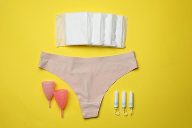 Photo of Flat lay composition with woman's panties and menstrual hygiene products on yellow background