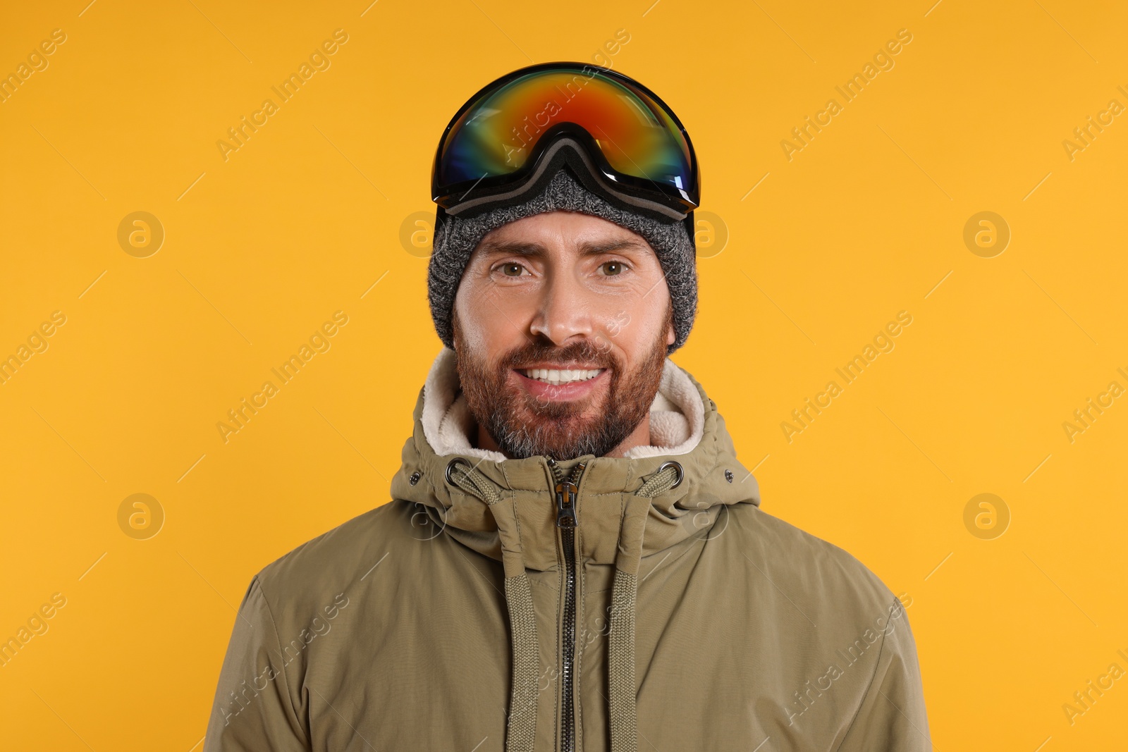 Photo of Winter sports. Happy man in ski suit and goggles on orange background