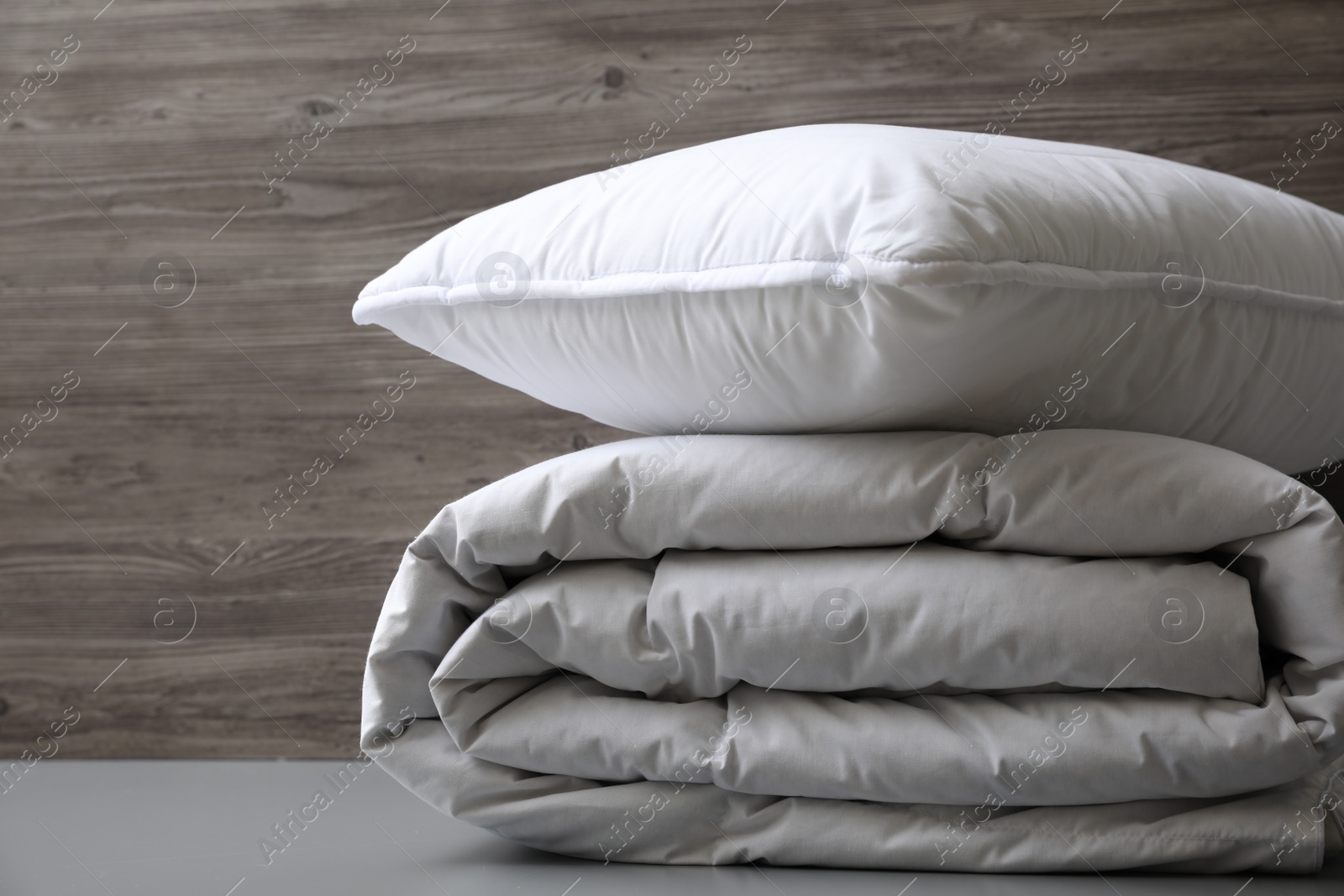 Photo of Soft folded blanket and pillow on light grey table, closeup