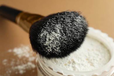 Makeup brush with rice loose face powder on brown background, closeup