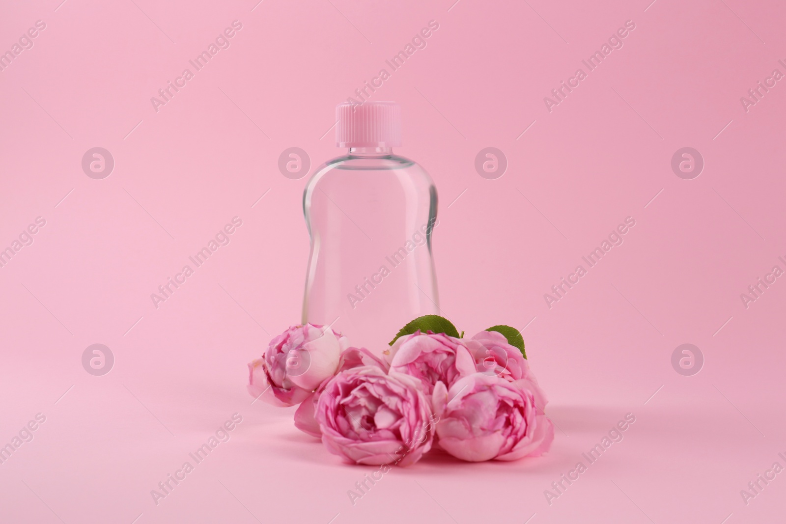Photo of Bottle with baby oil and beautiful flowers on pink background. Space for text
