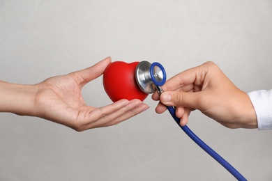 Photo of Doctor holding stethoscope near toy heart in patient's hand against grey background, closeup. Pulse checking