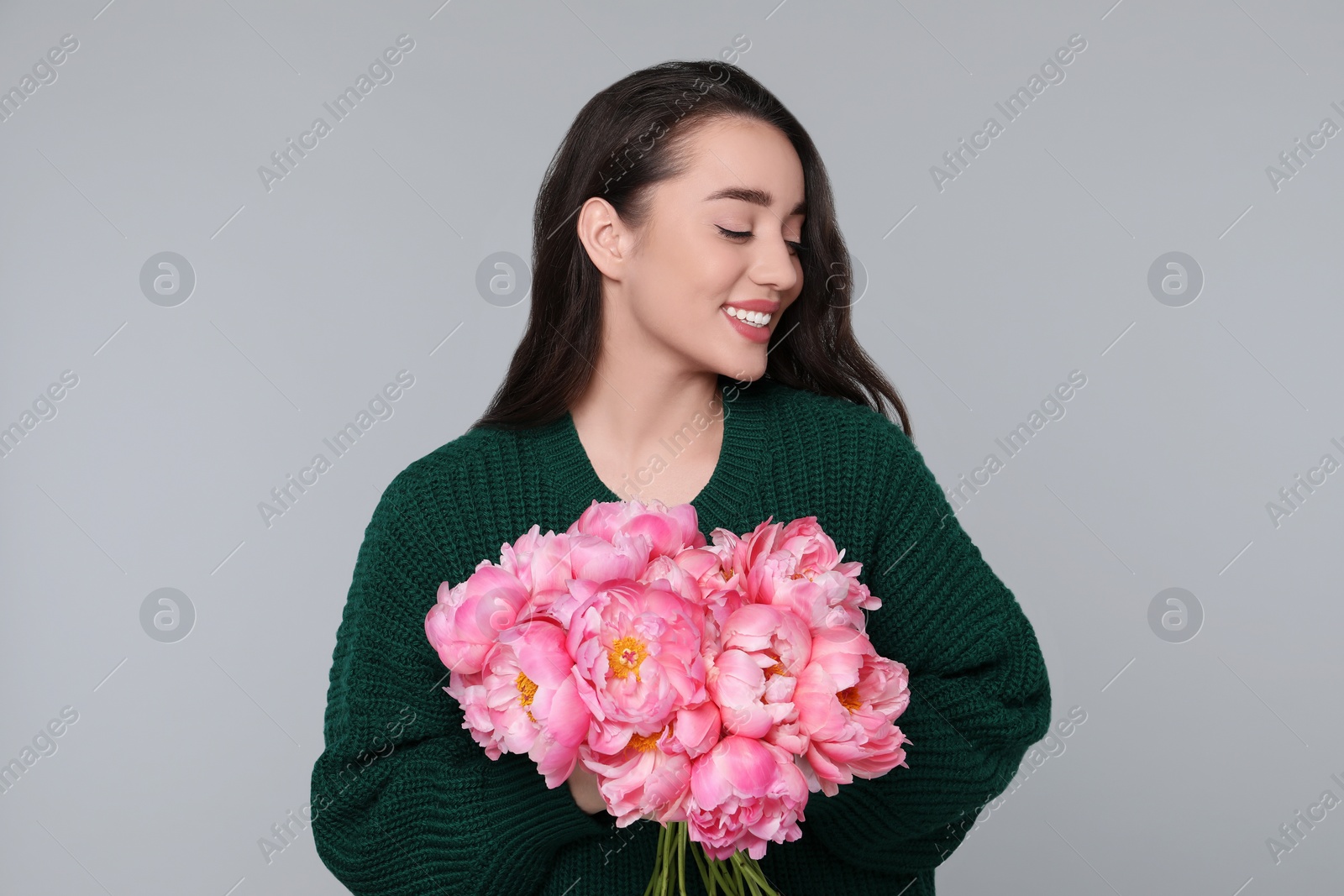 Photo of Beautiful young woman with bouquet of peonies on light grey background