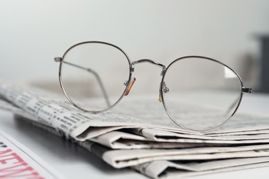 Stack of newspapers and glasses on white table indoors, closeup