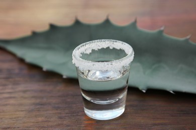 Mexican tequila shot with salt and green leaf on wooden table, closeup. Drink made of agava