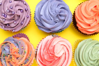 Photo of Delicious cupcake with bright cream on yellow background, flat lay