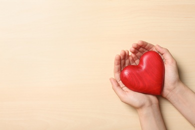 Photo of Woman holding heart on wooden background, top view with space for text. Donation concept