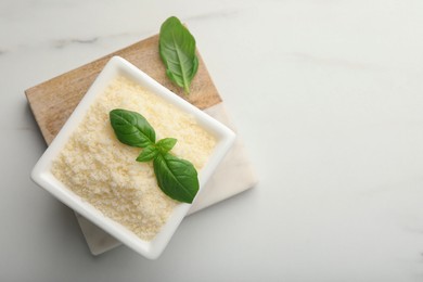 Photo of Square bowl with grated parmesan cheese and basil on white table, top view. Space for text