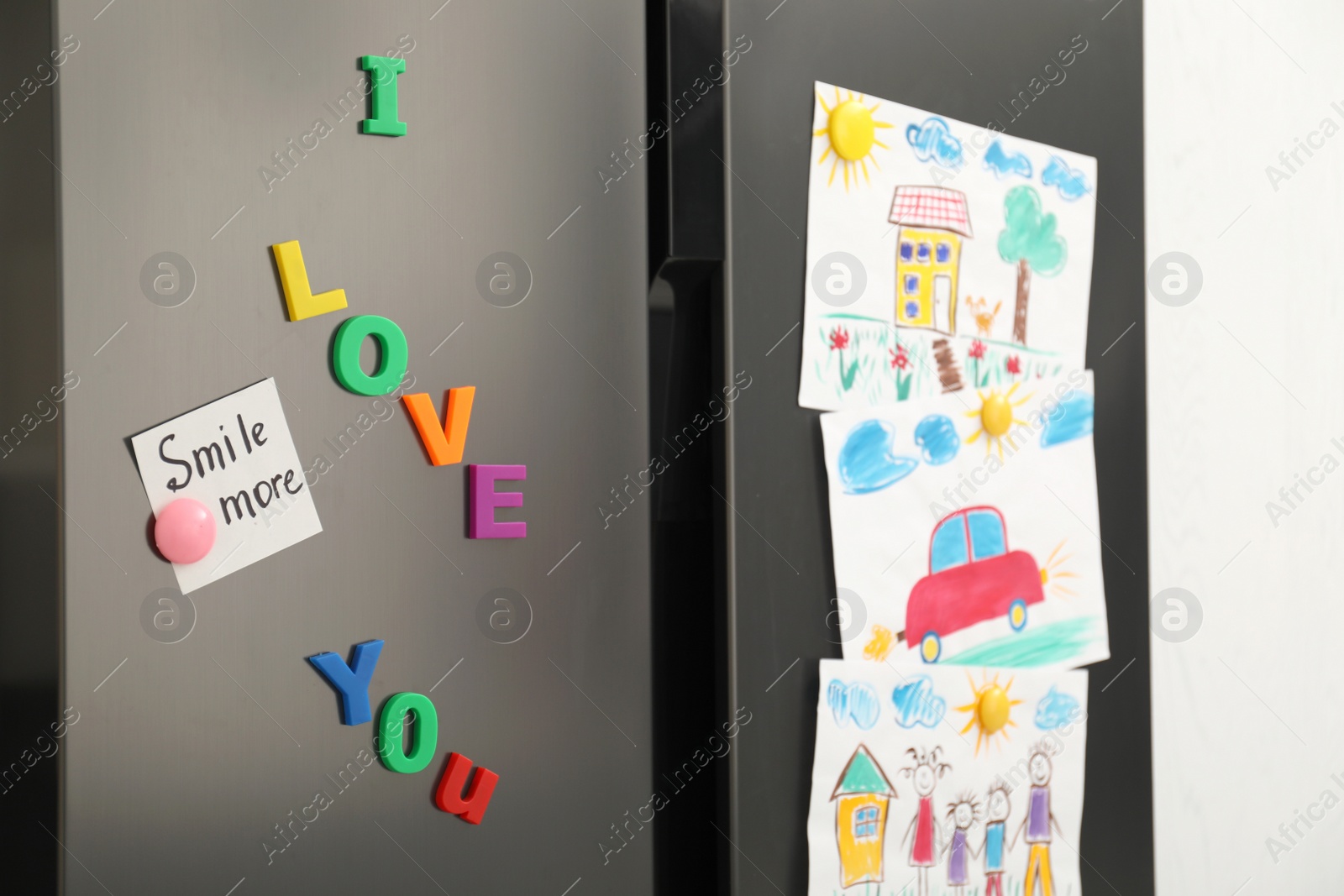 Photo of Modern refrigerator with child's drawings, note and magnets, closeup