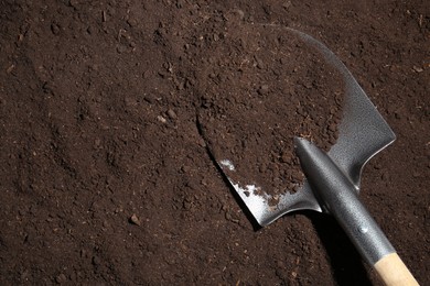 Photo of Metal shovel on fertile soil, top view and space for text. Gardening tool
