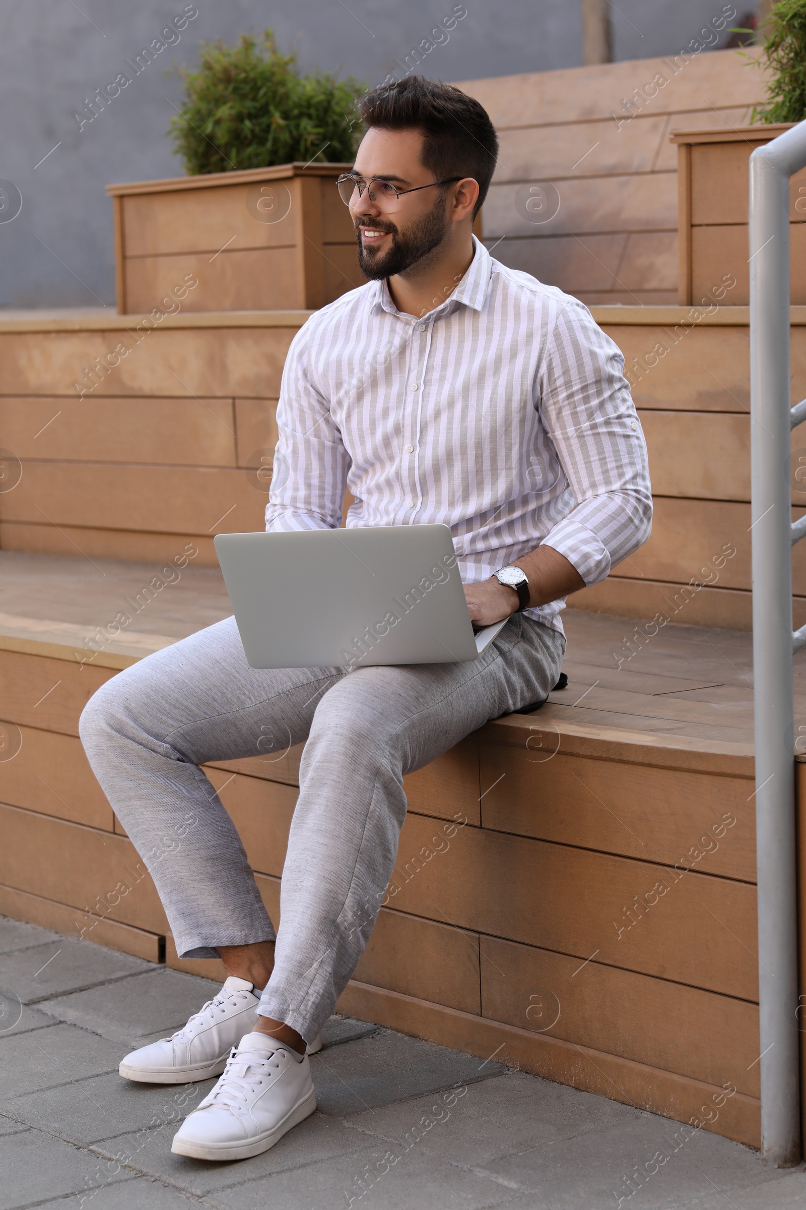 Photo of Handsome young man using laptop on bench outdoors