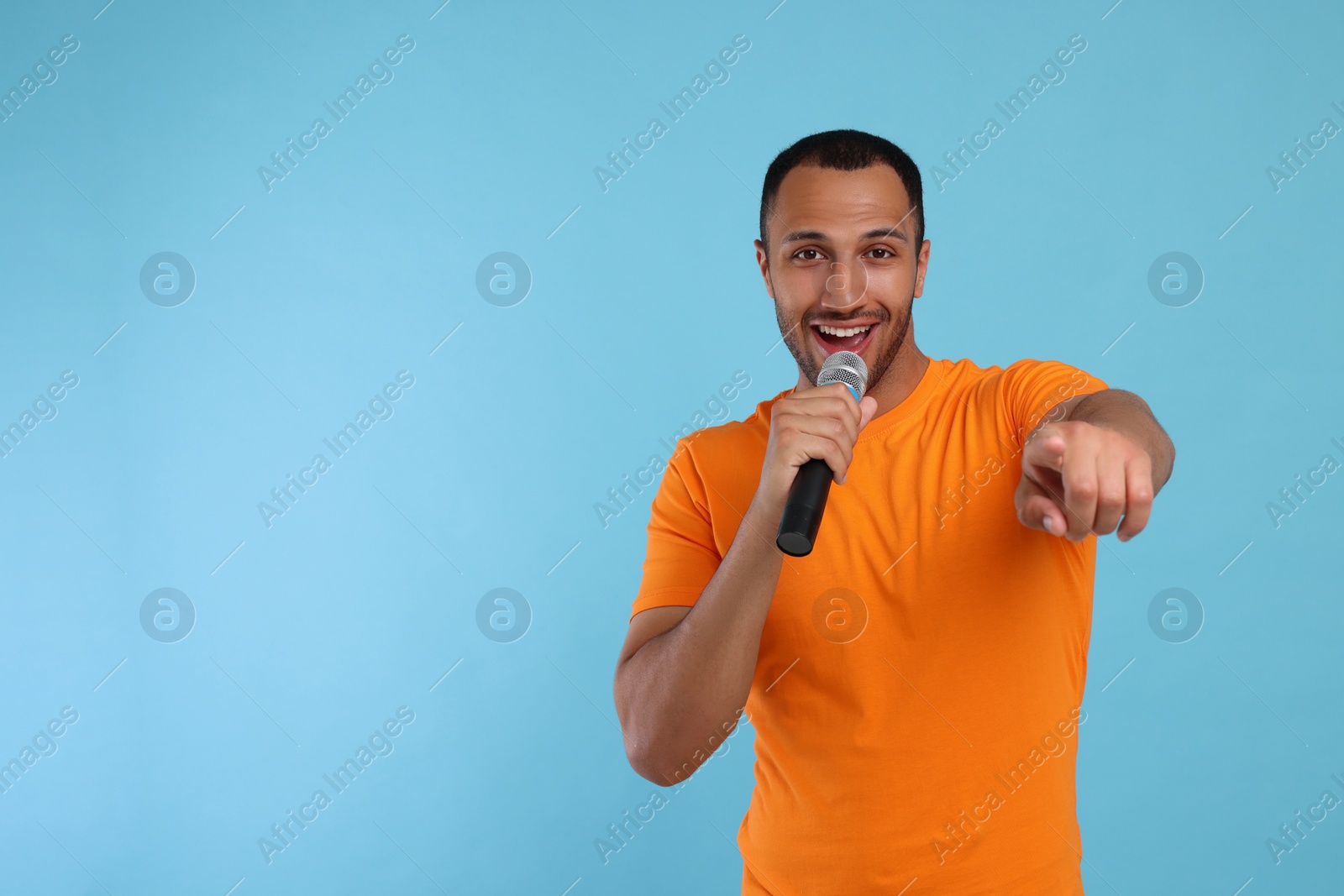 Photo of Handsome man with microphone singing on light blue background, space for text