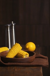 Photo of Plate with ripe corn cobs on table against dark background. Space for text