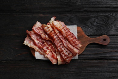 Slices of tasty fried bacon on black wooden table, top view