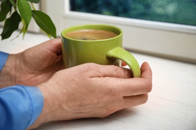 Photo of Woman with cup of hot coffee near window, closeup