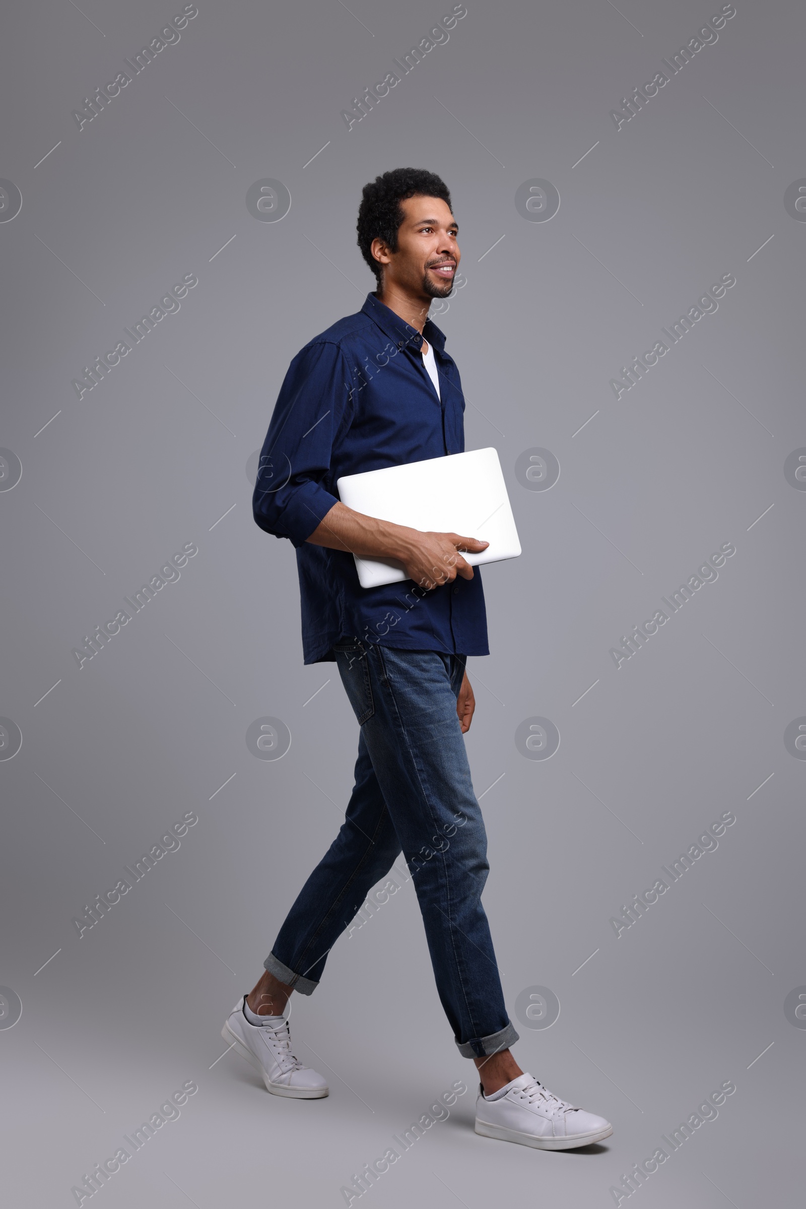 Photo of Happy man with laptop walking on grey background