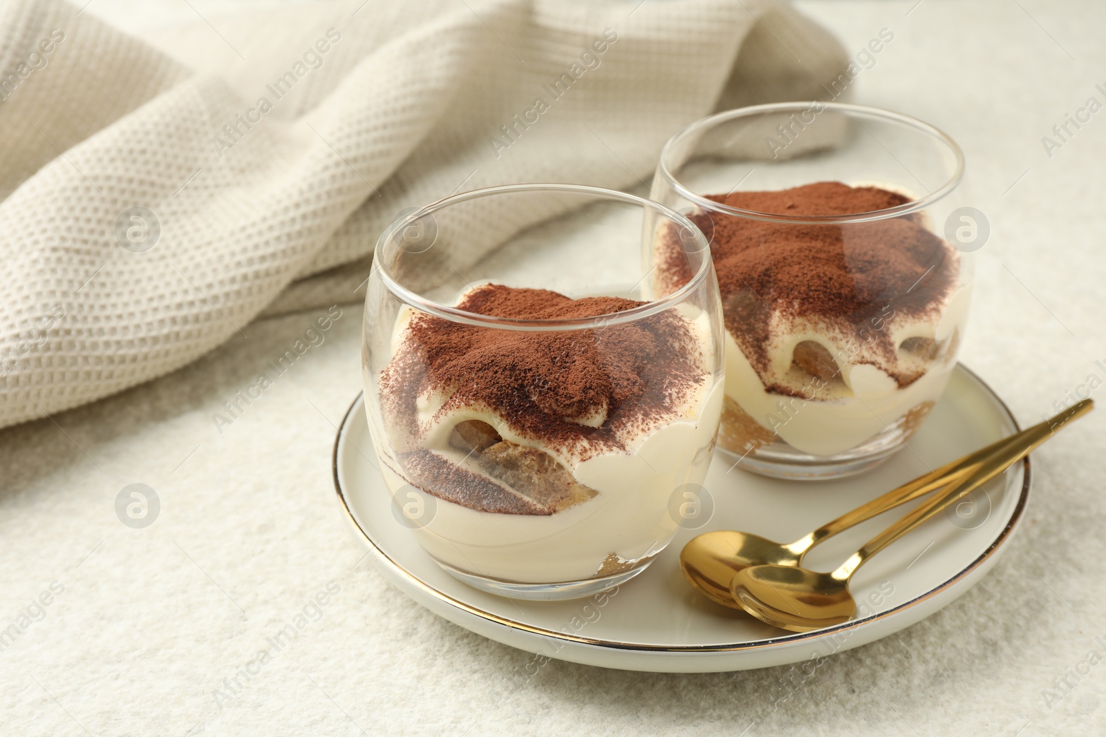 Photo of Delicious tiramisu in glasses and spoons on white table, space for text