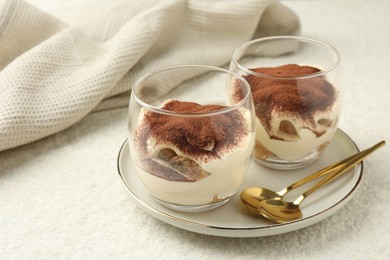 Delicious tiramisu in glasses and spoons on white table, space for text