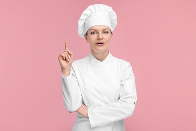 Photo of Happy chef in uniform pointing at something on pink background