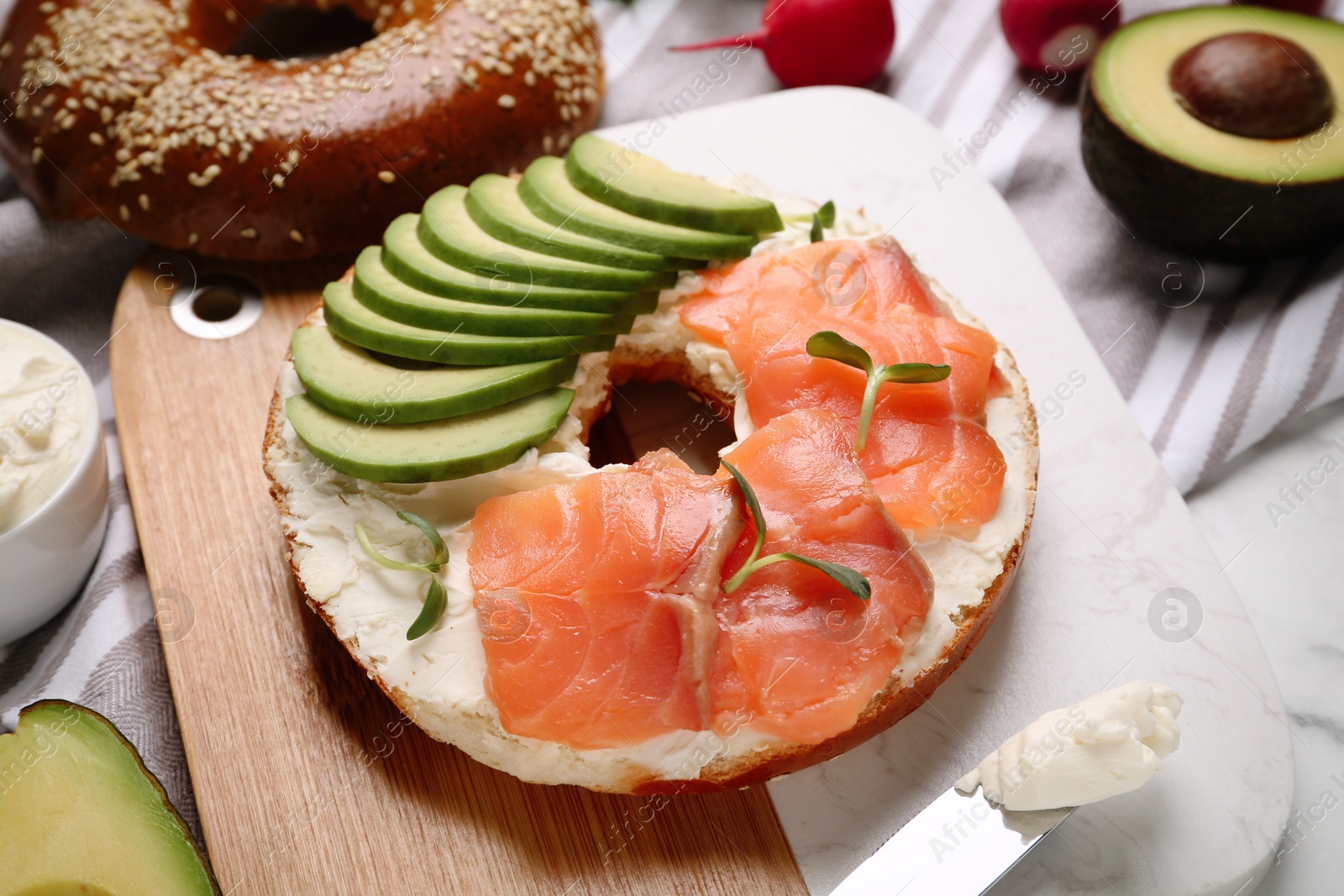 Photo of Delicious bagel with cream cheese, salmon and avocado on board, closeup