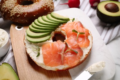 Photo of Delicious bagel with cream cheese, salmon and avocado on board, closeup