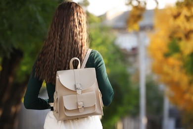 Young woman with stylish beige backpack in park, back view. Space for text