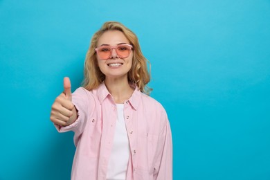 Photo of Happy young woman showing thumb up gesture on light blue background. Space for text