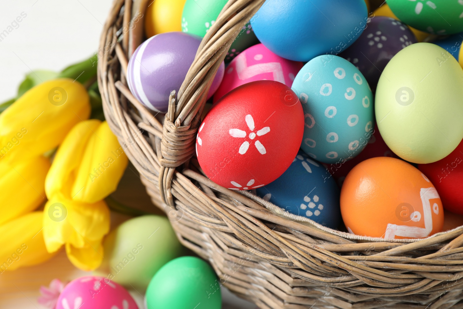 Photo of Colorful Easter eggs in wicker basket on white table, closeup