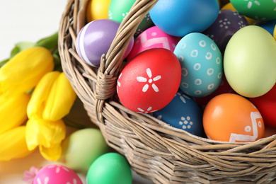 Photo of Colorful Easter eggs in wicker basket on white table, closeup