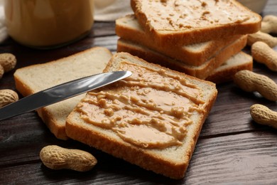 Photo of Delicious toasts with peanut butter, nuts and knife on dark wooden table, closeup